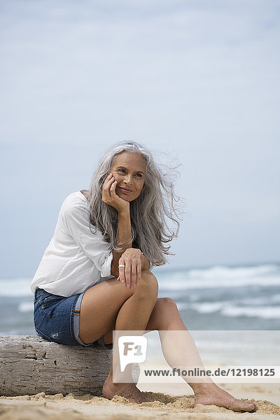 Schöne Seniorin am Strand sitzend
