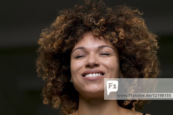 Porträt einer glücklichen Frau mit geschlossenen Augen vor schwarzem Hintergrund