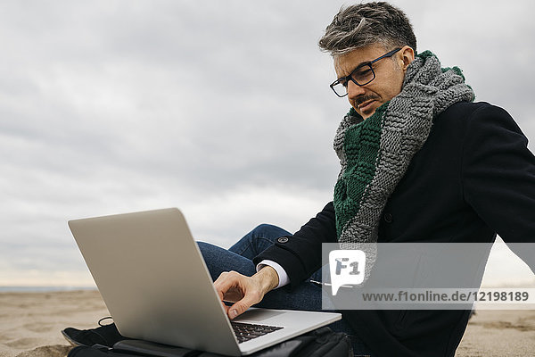 Businessman sitting on the beach in winter using laptop