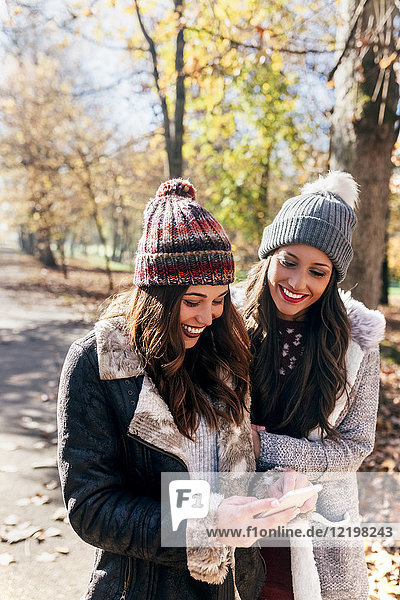 Two happy women with cell phone in autumnal forest