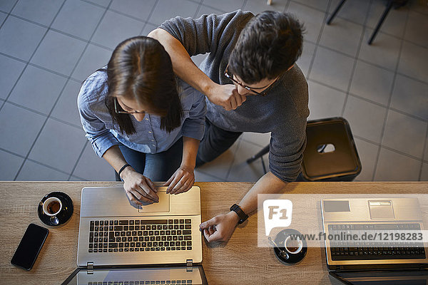 Draufsicht auf eine junge Frau und einen Mann in einem Café  die sich einen Laptop teilen.