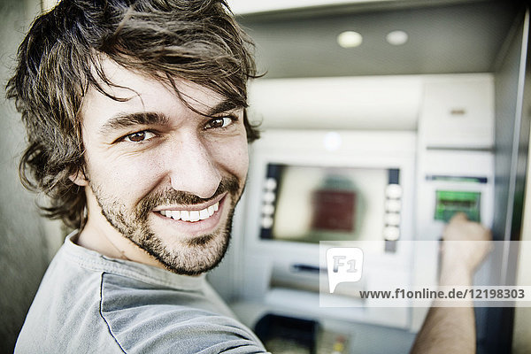 Porträt des lachenden jungen Mannes am Geldautomaten