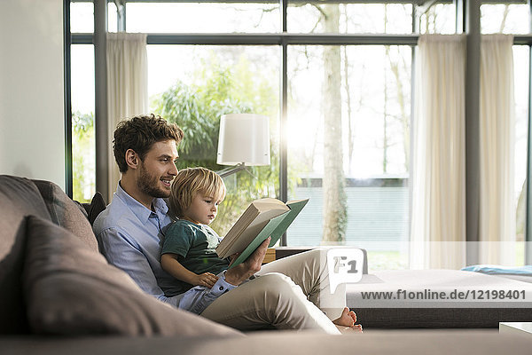 Father and son reading book on couch at home