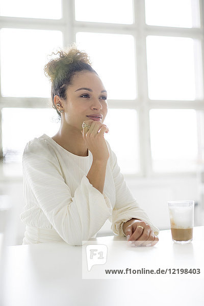 Portrait of smiling young woman sitting at table with glass of coffee