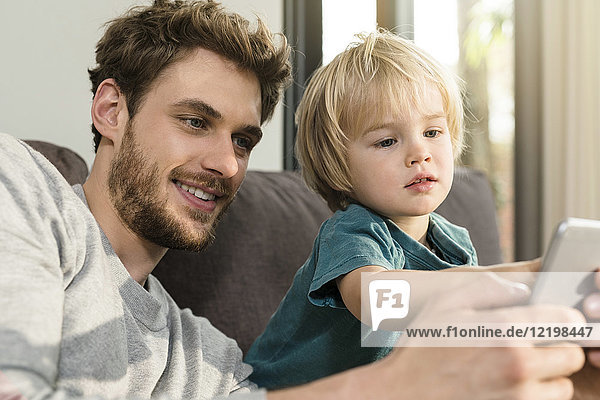 Vater und Sohn betrachten Smartphone auf der Couch zu Hause