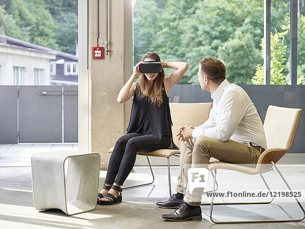 Mann schaut auf Frau mit VR-Brille auf Stuhl sitzend