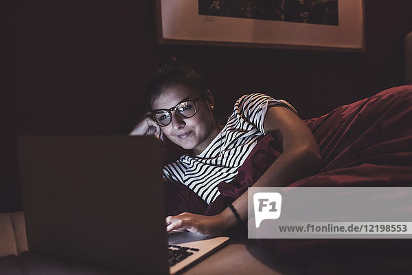 Woman lying in bed at home using laptop