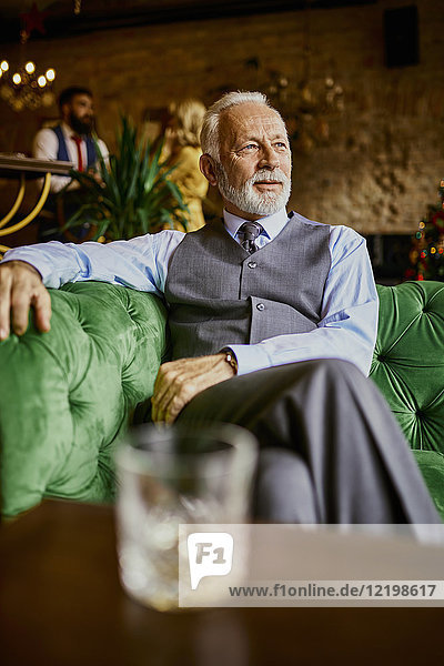 Portrait of elegant senior man sitting on couch in a bar