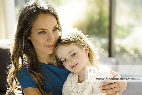 Portrait of smiling mother holding her daughter in front of window