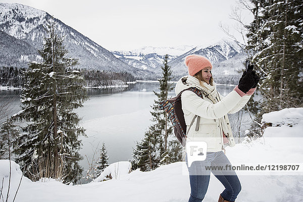 Junge Frau bei einem Selfie in alpiner Winterlandschaft mit See