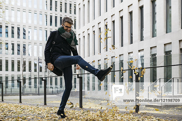Businessman playing with autumn leaves in the city