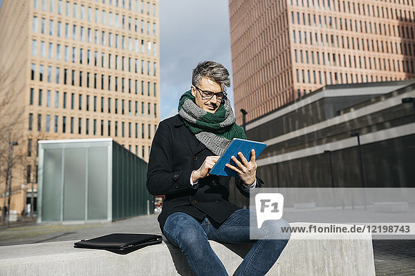 Businessman sitting on bench in the city using tablet