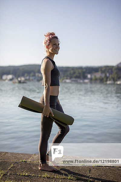 Frau in Sportbekleidung beim Wandern mit Yogamatte am Seeufer