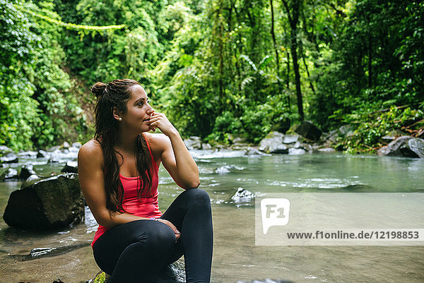 Costa Rica  Vulkan Arenal Nationalpark  Frau sitzt auf einem Stein des Flusses Fortuna