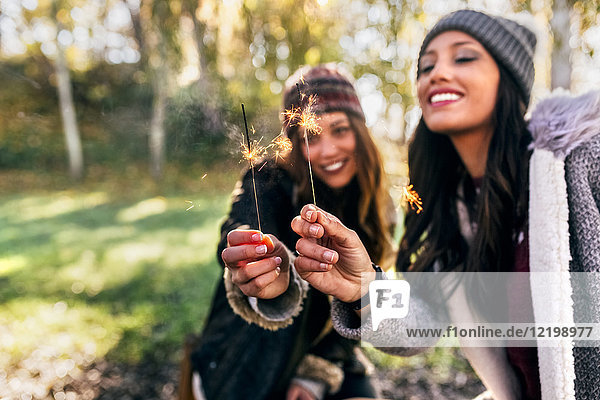 Two happy women holding sparklers in an autumnal forest