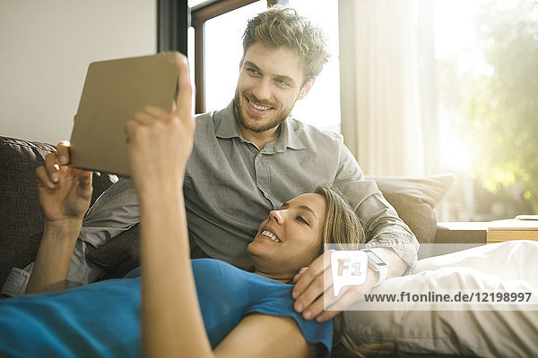 Smiling couple looking at tablet and relaxing on sofa at home