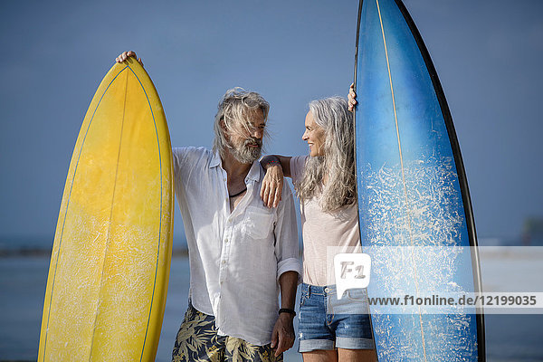 Liebevolles Seniorenpaar mit Surfbrettern am Strand
