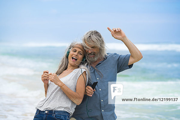 Hübsches Seniorenpaar mit Kopfhörern am Strand tanzend