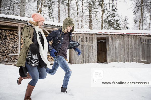 Happy couple running in front of wood pile outdoors in winter