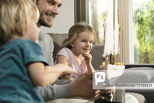Smiling father and children looking at toy model ship on couch at home