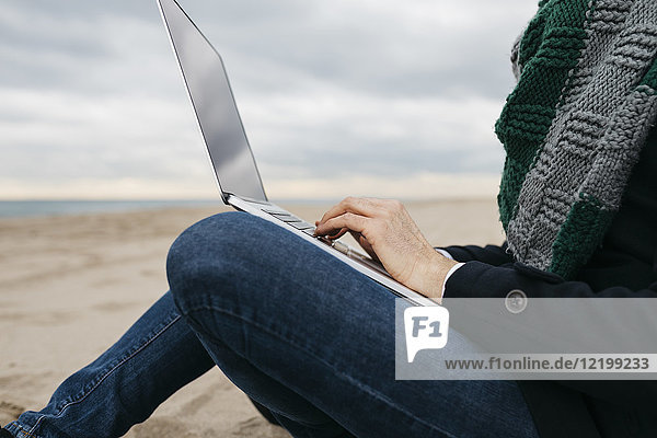 Businessman sitting on the beach in winter using laptop  partial view