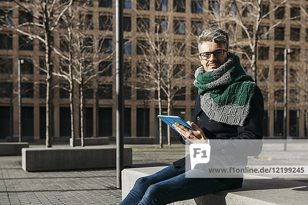 Businessman with tablet sitting on bench in the city in winter
