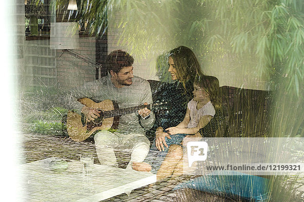 Happy parents and daughter playing guitar on sofa at home