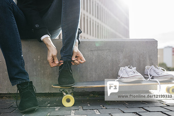 Freelancer with longboard sitting on bench tying his shoes  partial view