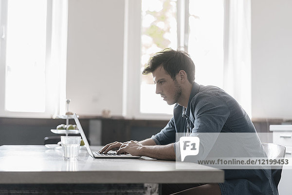 Junger Mann sitzt am Tisch und arbeitet am Laptop.