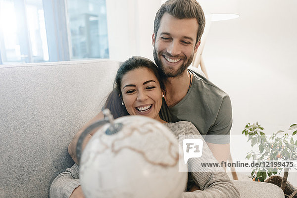 Glückliches Paar auf der Couch zu Hause mit Blick auf den Globus
