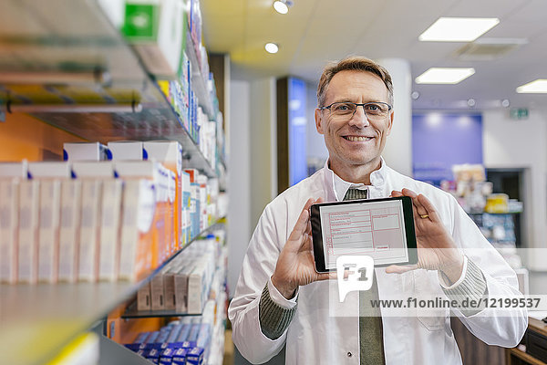 Portrait of smiling pharmacist in pharmacy holding tablet with digital prescription