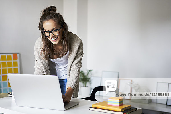 Happy young woman at home using laptop on desk