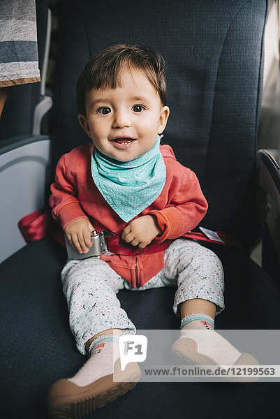 Baby sitzt auf einem Flugzeug neben dem Fenster mit Sicherheitsgurten