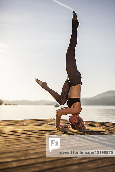 Frau praktiziert Yoga am Steg eines Sees mit Kopfstand