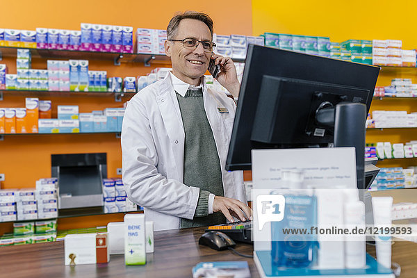 Smiling pharmacist talking on phone at counter in pharmacy