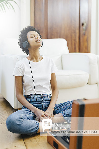 Young woman sitting on grounf listening music from record player  using headphones