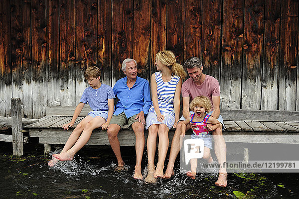 Familie sitzt zusammen auf einem Steg und spritzt mit Wasser.