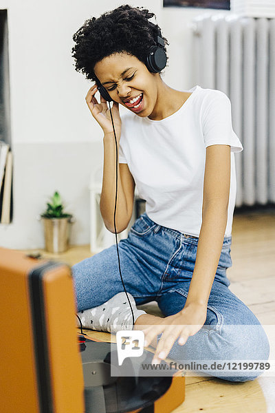 Young woman sitting on grounf listening music from record player  using headphones