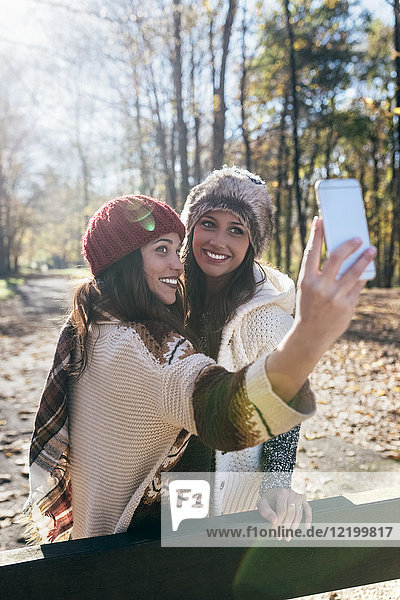 Zwei hübsche Frauen  die einen Selfie in einem herbstlichen Wald nehmen.