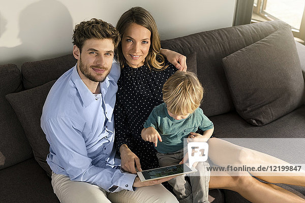 Porträt der lächelnden Eltern und des Sohnes auf dem Sofa mit Tablette zu Hause
