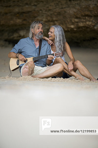 Schönes älteres Paar  das am Strand sitzt und Gitarre spielt.