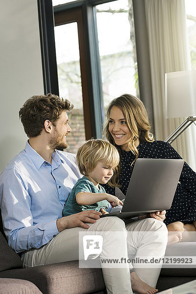 Smiling parents and son sitting on sofa with laptop at home