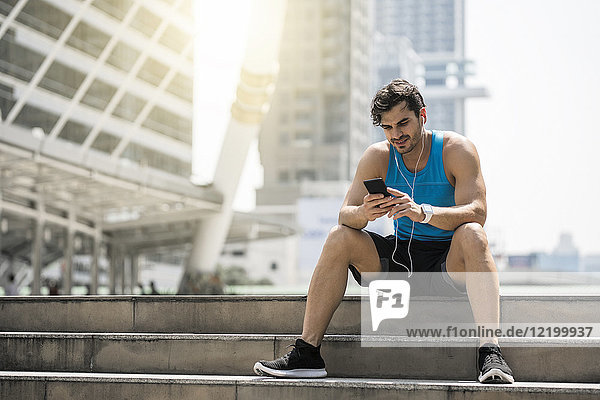 Runner wearing earphones  checking messages on his smartphone