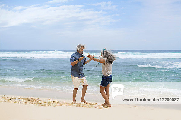 Handsome senior couple with headphones dancing on the beach
