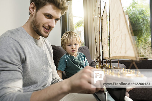 Father and son looking at toy model ship on couch at home