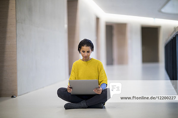 Porträt einer jungen Frau mit gelbem Pullover auf dem Boden sitzend mit Laptop