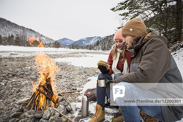 Couple on a trip in winter having a break at camp fire