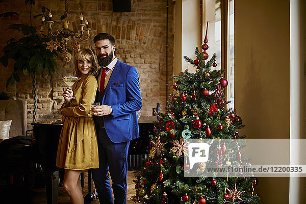Portrait of elegant couple with drinks at Christmas tree