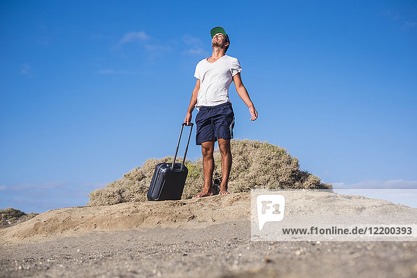 Man standing with rolling suitcase at the beach