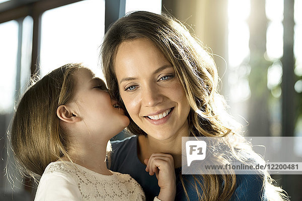 Lächelndes Mädchen flüstert ihrer Mutter ins Ohr.